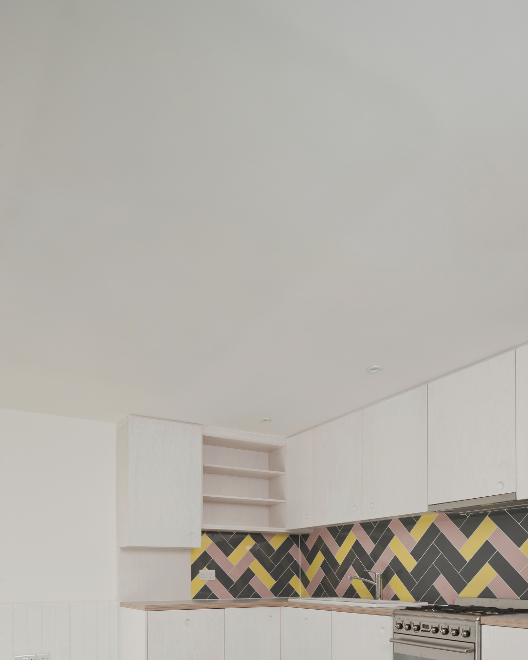A gloomy looking kitchen with white walls and a yellow-grey backsplash