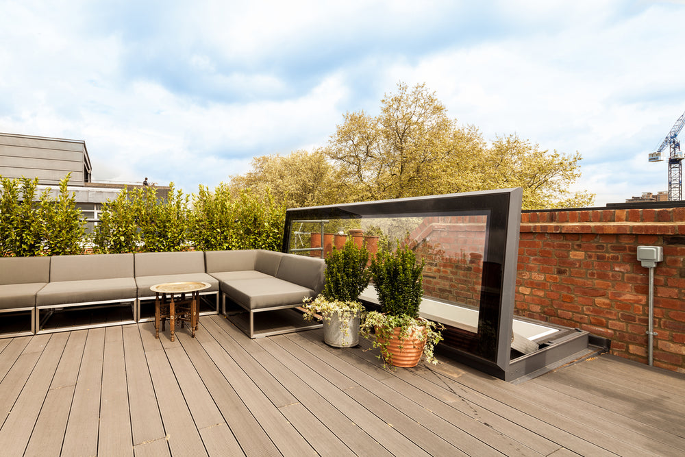 door style rooflight open on a roof terrace with wooden decking nd a brick wall to the right