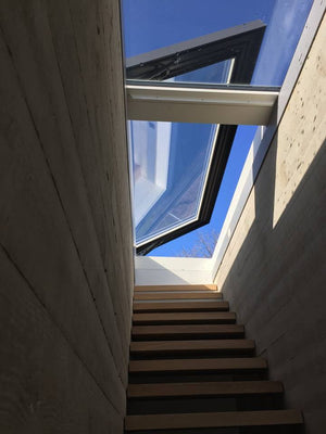 an open rooflight at the top of a wooden staircase, blue sky seen through